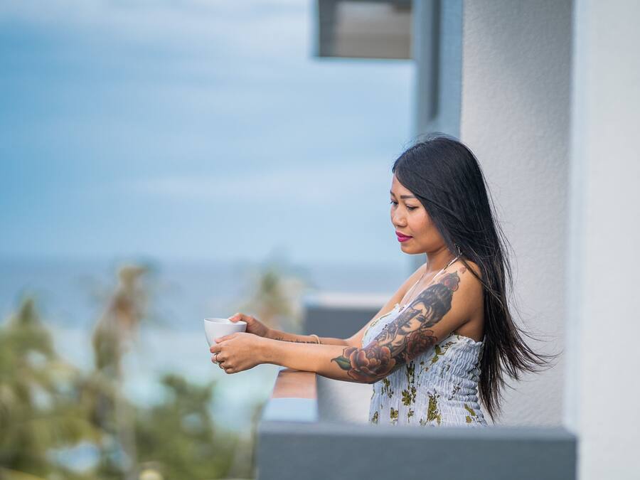 A person holding a cup, standing by a building with a view of the ocean.