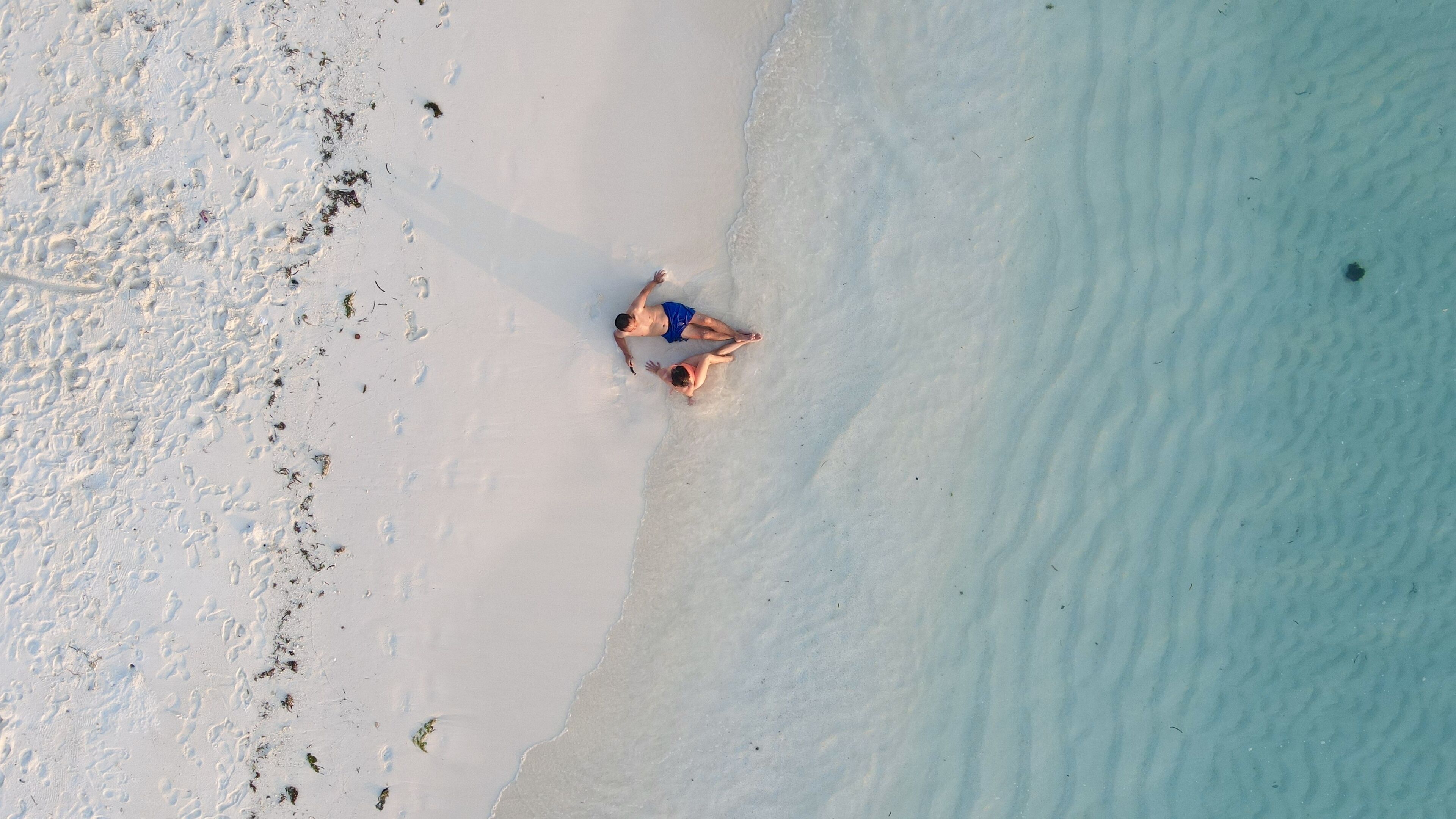 An aerial view of a beach with footprints and a person lying on the sand.