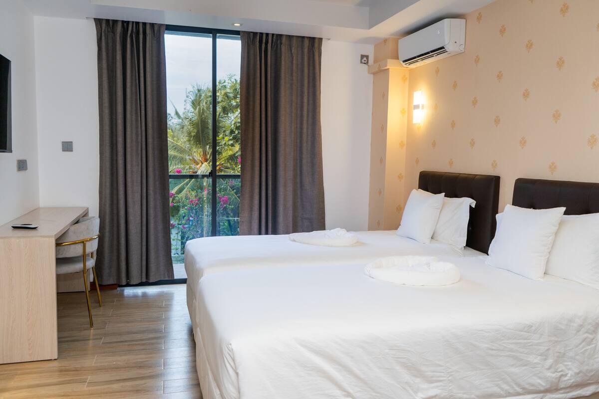 A hotel room with a large bed, a desk, and a balcony with curtains.