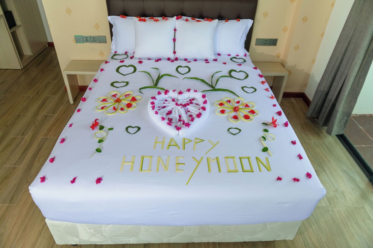 Una cama con una colcha blanca adornada con corazones y la frase 'HAPPY HONEYMOON'.