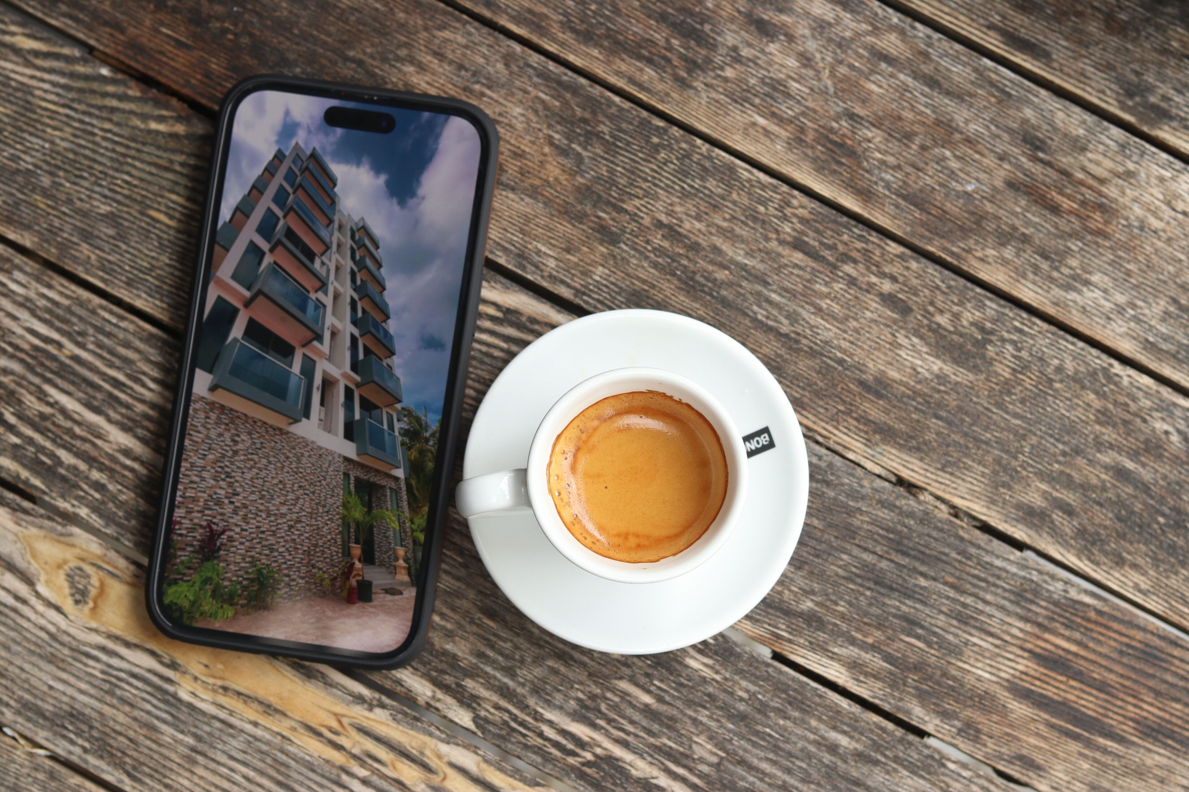 A smartphone displaying a building, a cup of coffee, and a wooden surface.