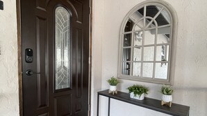 Eine dunkelbraune Tür mit Fensterglas, ein kleiner Beistelltisch mit Topfpflanzen und eine Fußmatte mit der Aufschrift "so happy you're here".