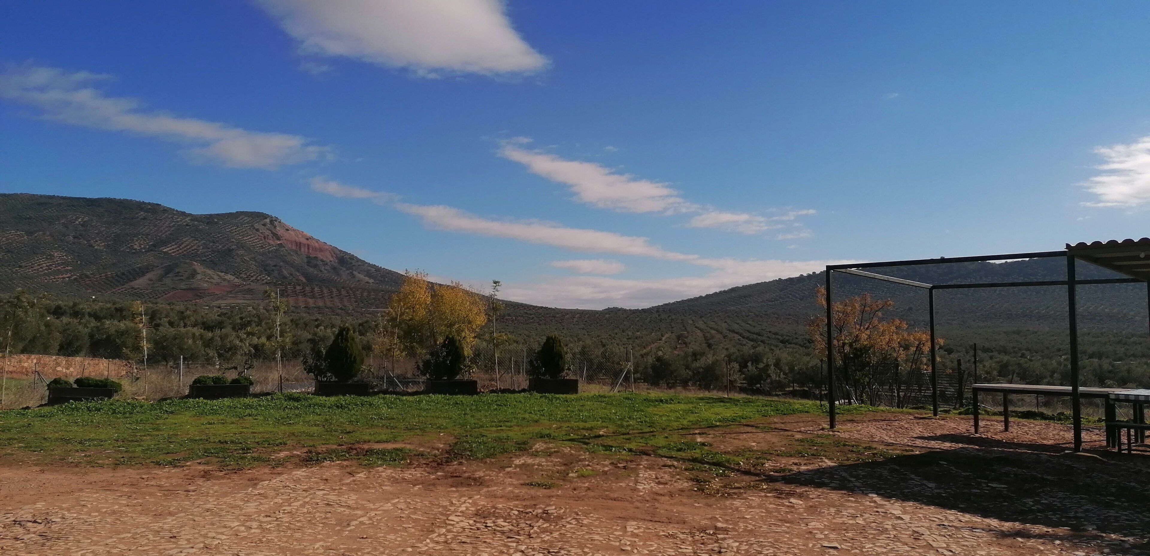 Un paysage rural avec un ciel dégagé, une montagne en arrière-plan et un espace extérieur abrité avec une table et des chaises.