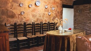 Un interior rústico con pared de piedra, bancos de madera, una mesa redonda con un florero y flores, además de una pared de ladrillo.