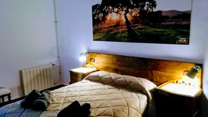 Un dormitorio con una cama, dos mesitas de noche con lámparas, un radiador y un cuadro colgado en la pared.