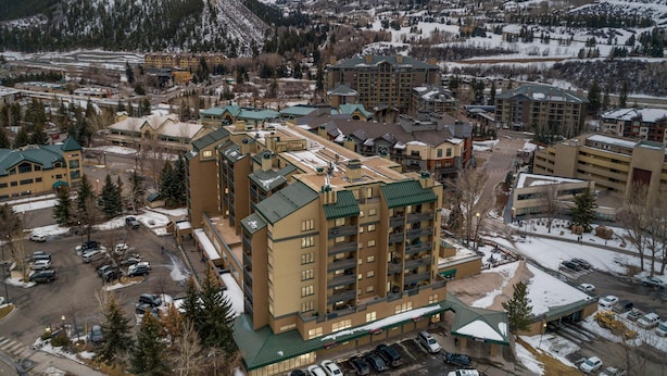 Een meerhoog hotel met een groen dak, omringd door met sneeuw bedekte bergen en een parkeerplaats.