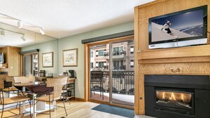 Un salon moderne avec une cheminée, un téléviseur fixé au mur et un coin repas aménagé avec des meubles en osier.