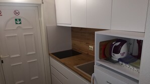 Une cuisine compacte avec un réfrigérateur blanc, un four à micro-ondes et un évier. On y trouve une porte avec un panneau « interdiction de fumer » et un panneau indiquant la sortie de secours.