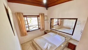 Un dormitorio con una cama grande, una ventana con cortinas, un espejo y suelo de baldosas.
