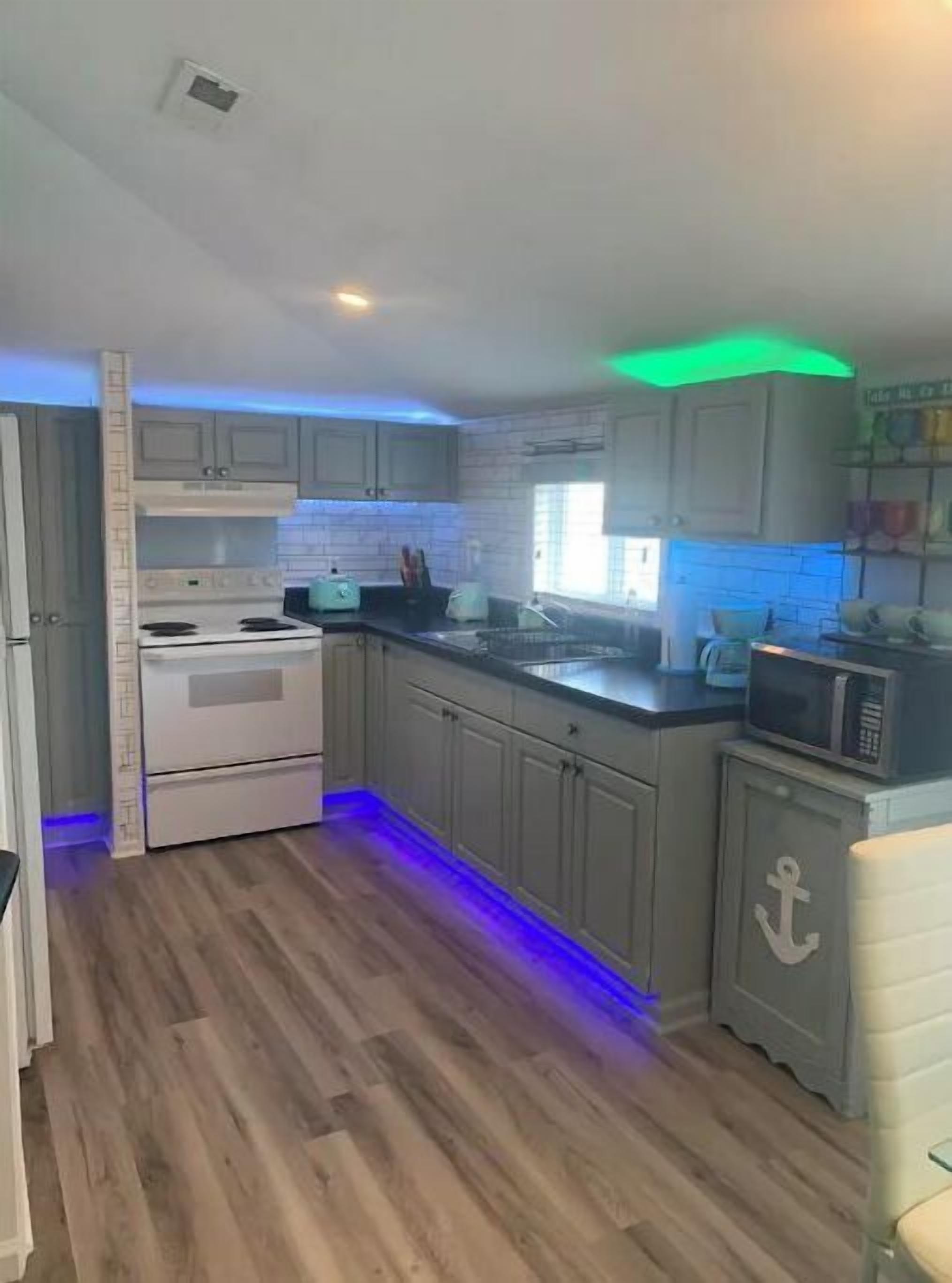 A kitchen with wooden flooring, white cabinets, a stove, and a microwave.