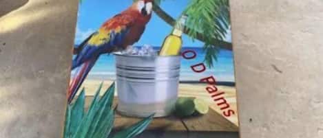 A painted metal surface with a tropical beach scene, including a parrot and a bucket.