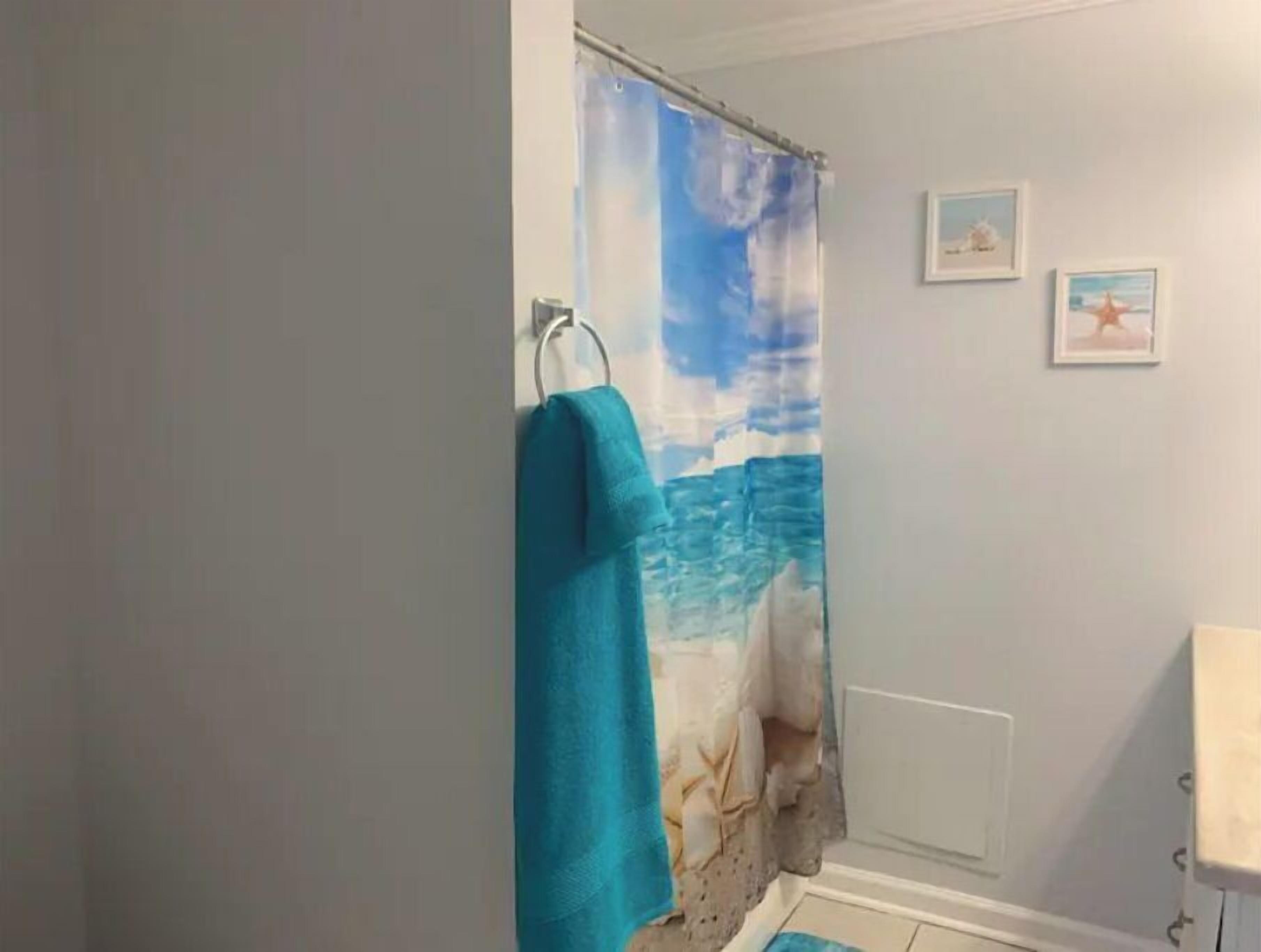 Ein Badezimmer mit Duschvorhang mit Strandmotiv, einem an der Wand hängenden Handtuch und zwei gerahmten Bildern.