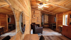 Ein Interieur einer Holzhütte mit Essbereich, einer Couch, einem Deckenventilator und einer Gitarre an der Wand.