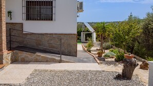 A building with a stone staircase leading to a gated entrance, a covered outdoor area with a pergola, and a view of a hilly landscape.