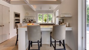A modern kitchen with two bar stools, a central island, and a large window providing a view of the outdoors.