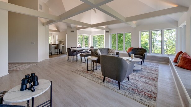 A spacious living area with a high ceiling, large windows, and a mix of seating arrangements including a sofa and chairs.