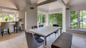 A modern kitchen with a dining area, large windows, and a view of trees.