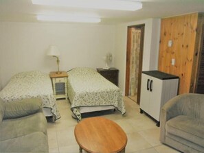 A small, clean room with two single beds, a wooden table, a sofa, a cabinet, and a fan. - Sea Breeze (Wells)