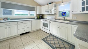 A kitchen with white cabinets, a stove, a microwave, and a window with a view of greenery.