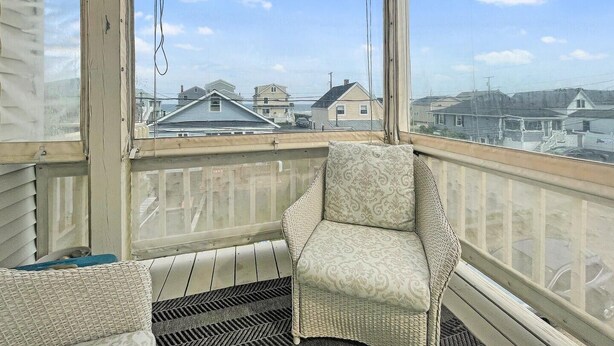 A covered balcony with wicker furniture and a view of neighboring houses.