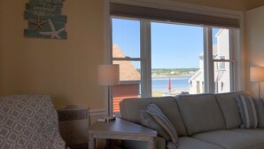 A cozy living room with a view of the sea, a patterned armchair, a small table, and a couch with striped pillows.