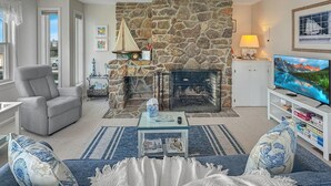 Una sala de estar con chimenea de piedra, un sillón gris, una mesa de centro y un televisor.