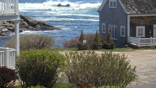 Una casa costera con un porche, una orilla rocosa y olas rompiendo cerca.