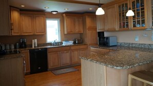 Une cuisine dotée de meubles en bois, de plans de travail en granit, d’un lave-vaisselle, d’un four à micro-ondes et de luminaires suspendus.