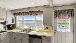 A kitchen with a sink, stove, and dishwasher. There are windows with curtains and a view of the outside. - Sweet Dreams (Wells)