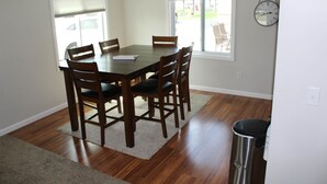 A dining area with a wooden table and chairs, a trash can, and a clock on the wall. - Jack's on the Bay, 3 Bedroom/1 Bath (Denton Township)