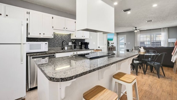 Une cuisine moderne avec des meubles blancs, des plans de travail en granit et un îlot central doté de tabourets.