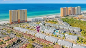 Une vue aérienne d’une zone de villégiature comprenant plusieurs bâtiments, une plage et un ciel bleu dégagé.