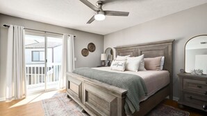 Une chambre avec un grand lit, un ventilateur de plafond, une table de chevet et une vue sur l’extérieur.