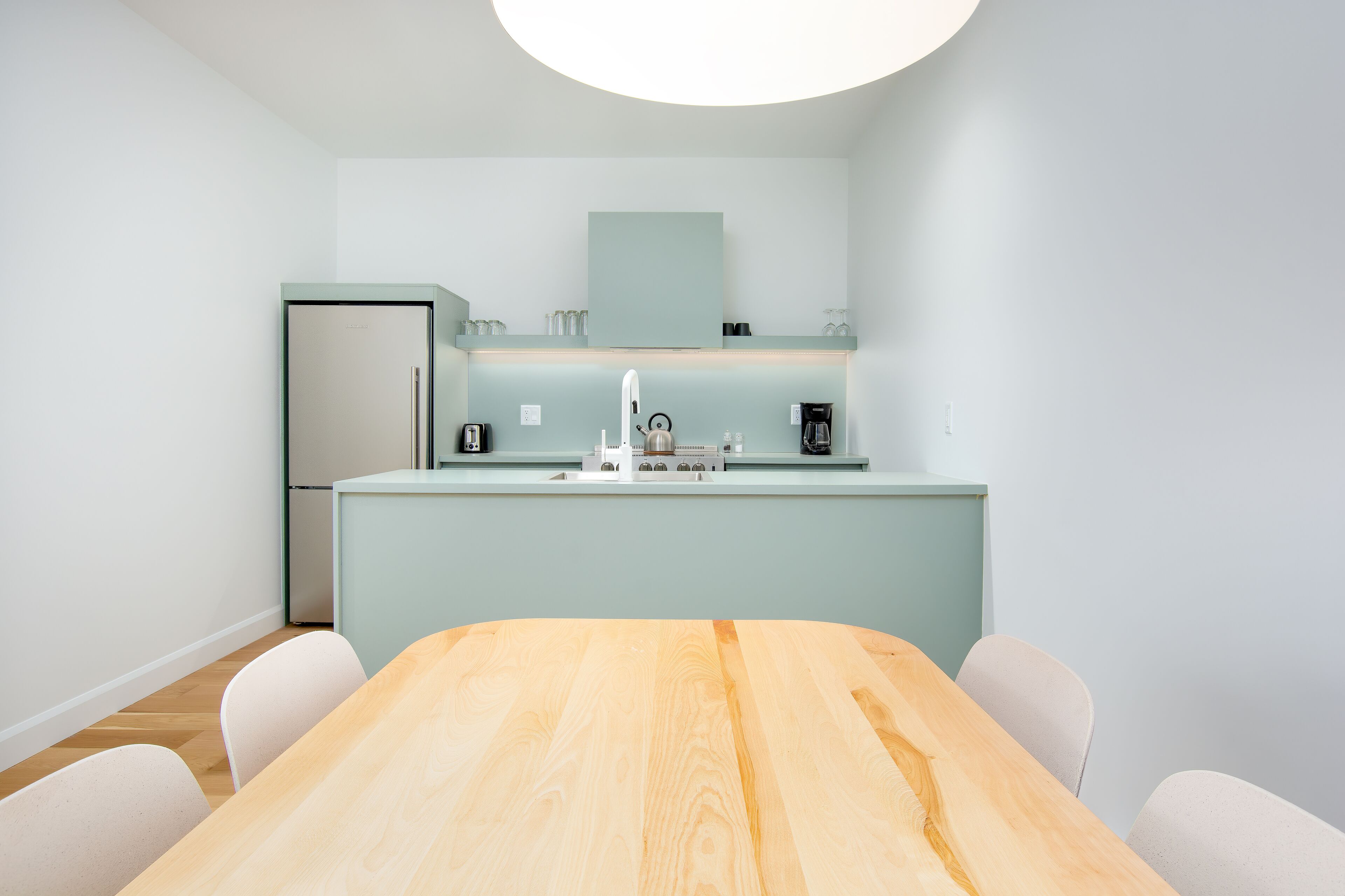 Een moderne keuken met een centraal eiland, witte stoelen en een houten tafel.