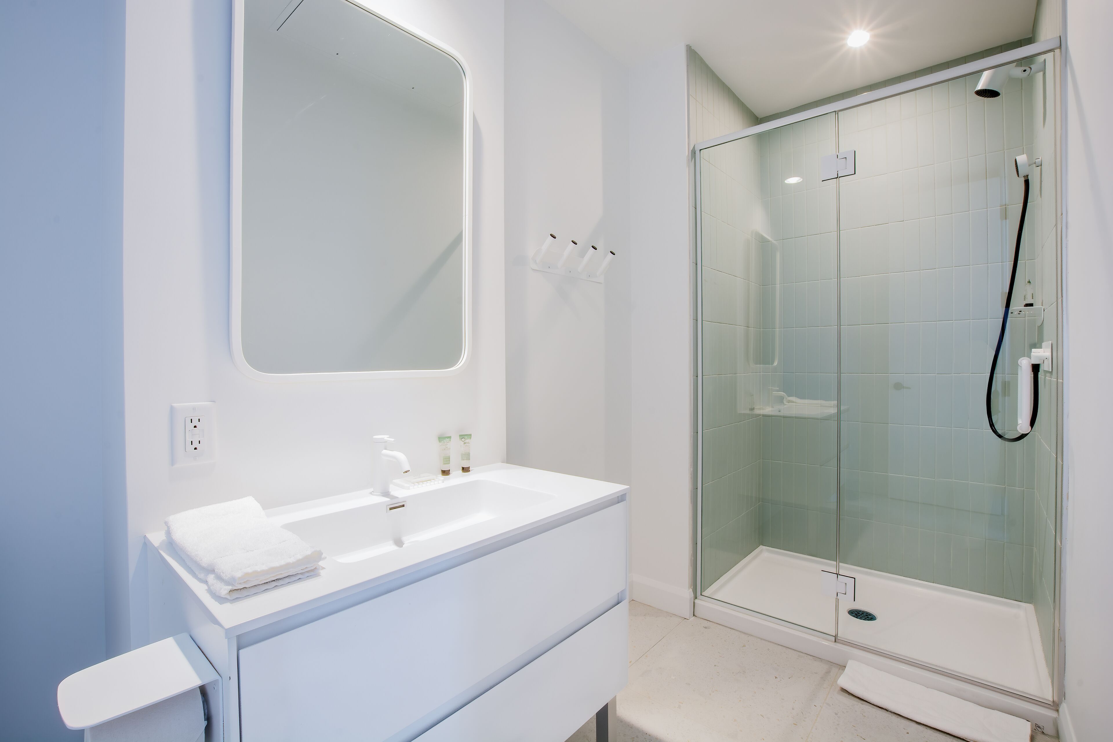 A modern bathroom with a white vanity, a large mirror, and a glass-enclosed shower.
