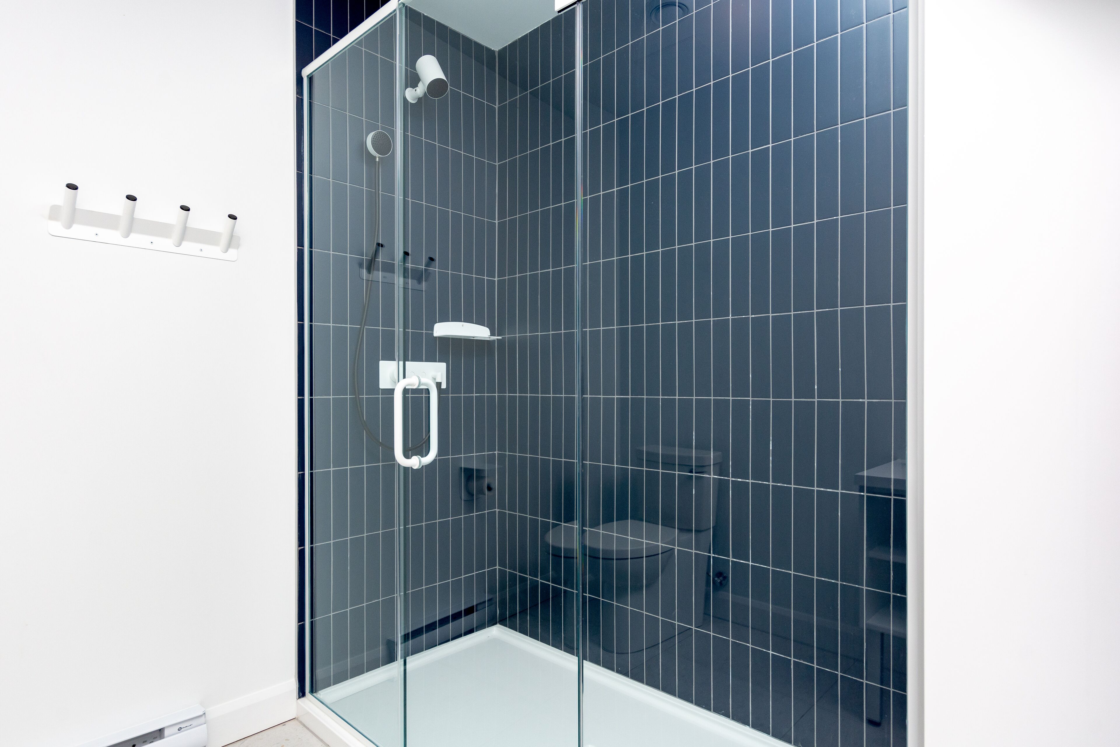 A modern bathroom with a glass-enclosed shower, white fixtures, and dark tiled walls.