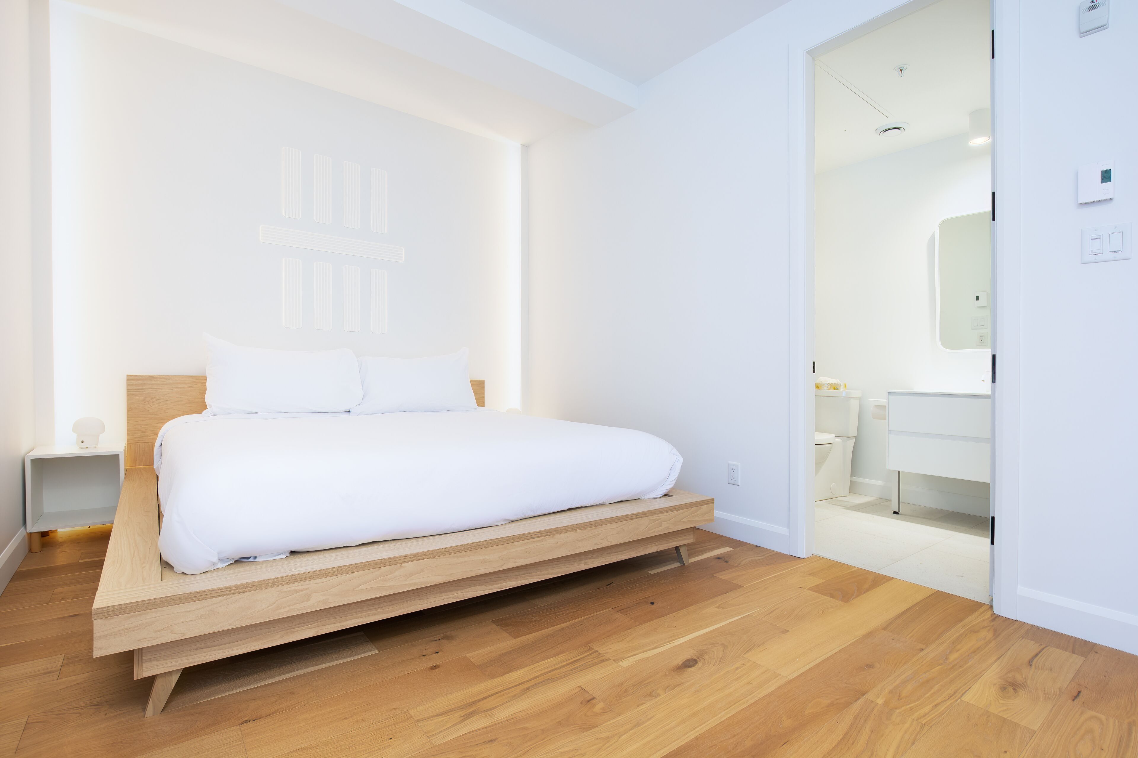A modern bedroom with a wooden platform bed, white bedding, and a minimalist design.