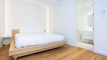 A modern bedroom with a wooden platform bed, white bedding, and a minimalist design.