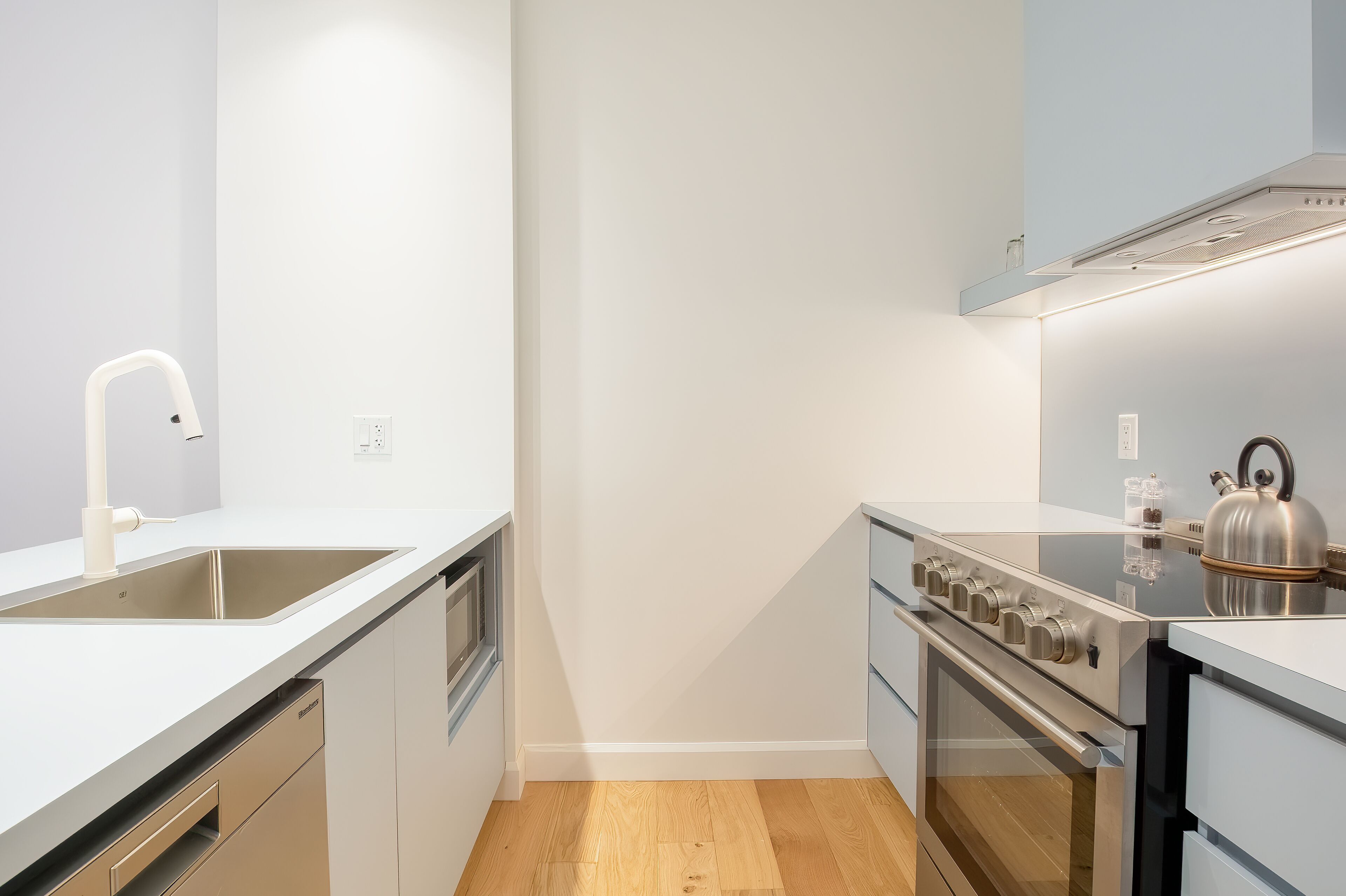 A modern kitchen with a stainless steel stove, a white sink, and wooden flooring.