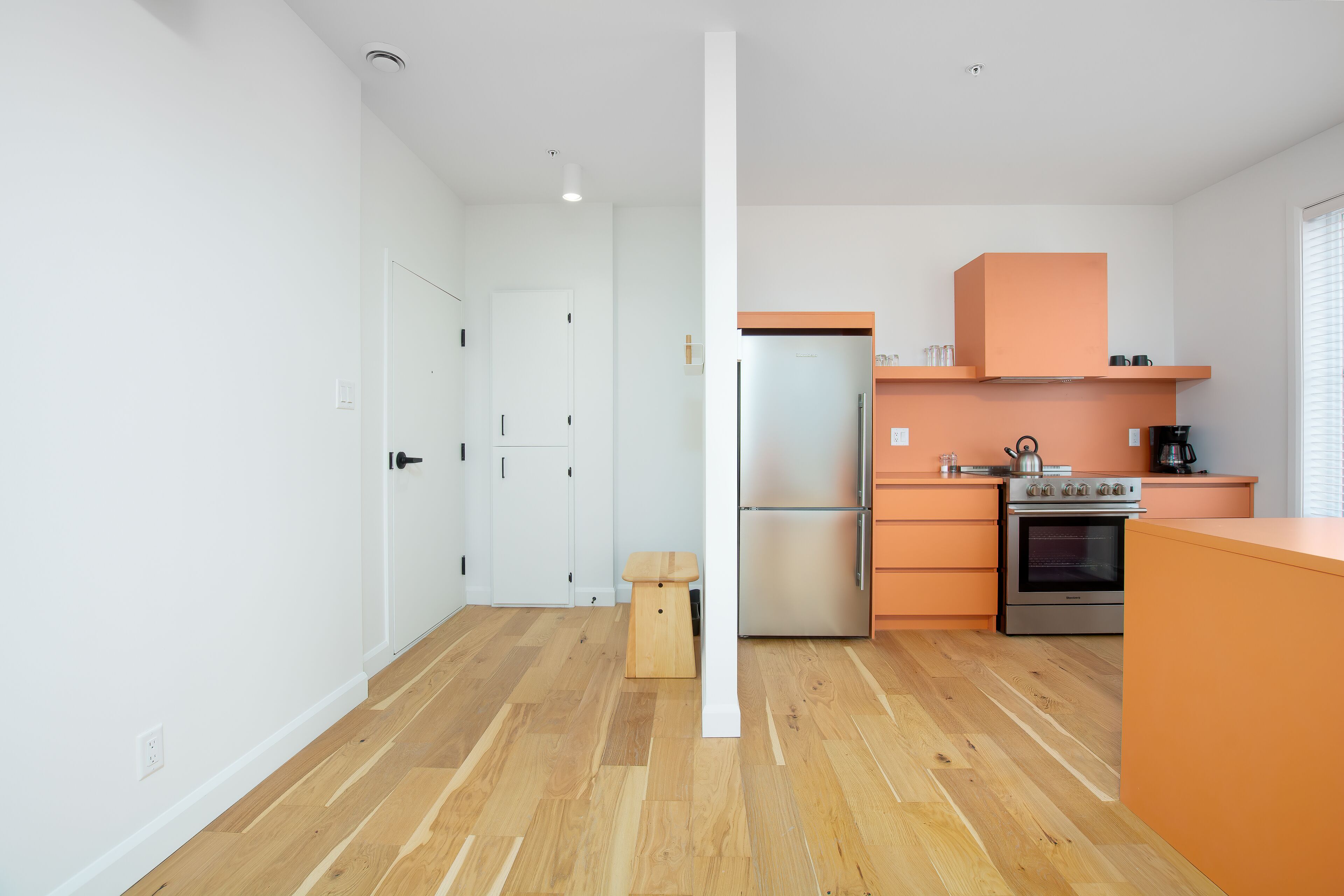 Une cuisine moderne avec un plancher en bois, des murs blancs et des meubles de couleur orange.