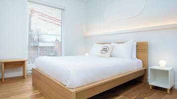 A modern bedroom with a wooden bed, white bedding, a bedside table, and a nightstand with a lamp.