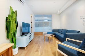 Un saló modern amb un sofà modular, un televisor de pantalla plana, una taula de centre i una planta gran.