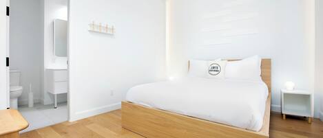 A modern bedroom with a wooden bed, white walls, and a wooden floor.