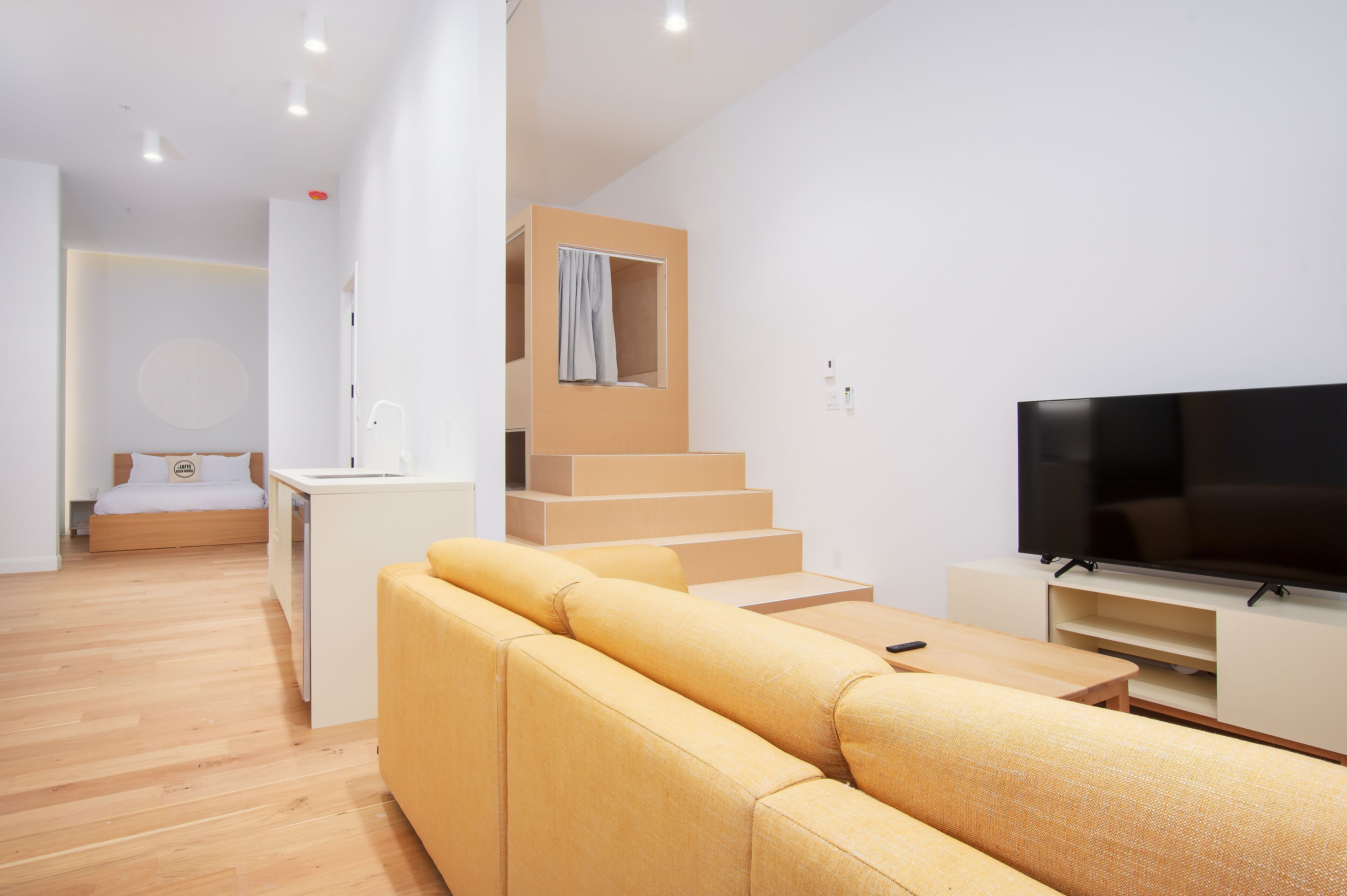 A modern living room with a sofa, a TV, and a staircase leading to a bedroom.