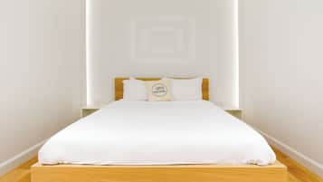 A neatly made bed with white bedding and a pillow with a logo, a wooden headboard, and a white wall with a geometric design.