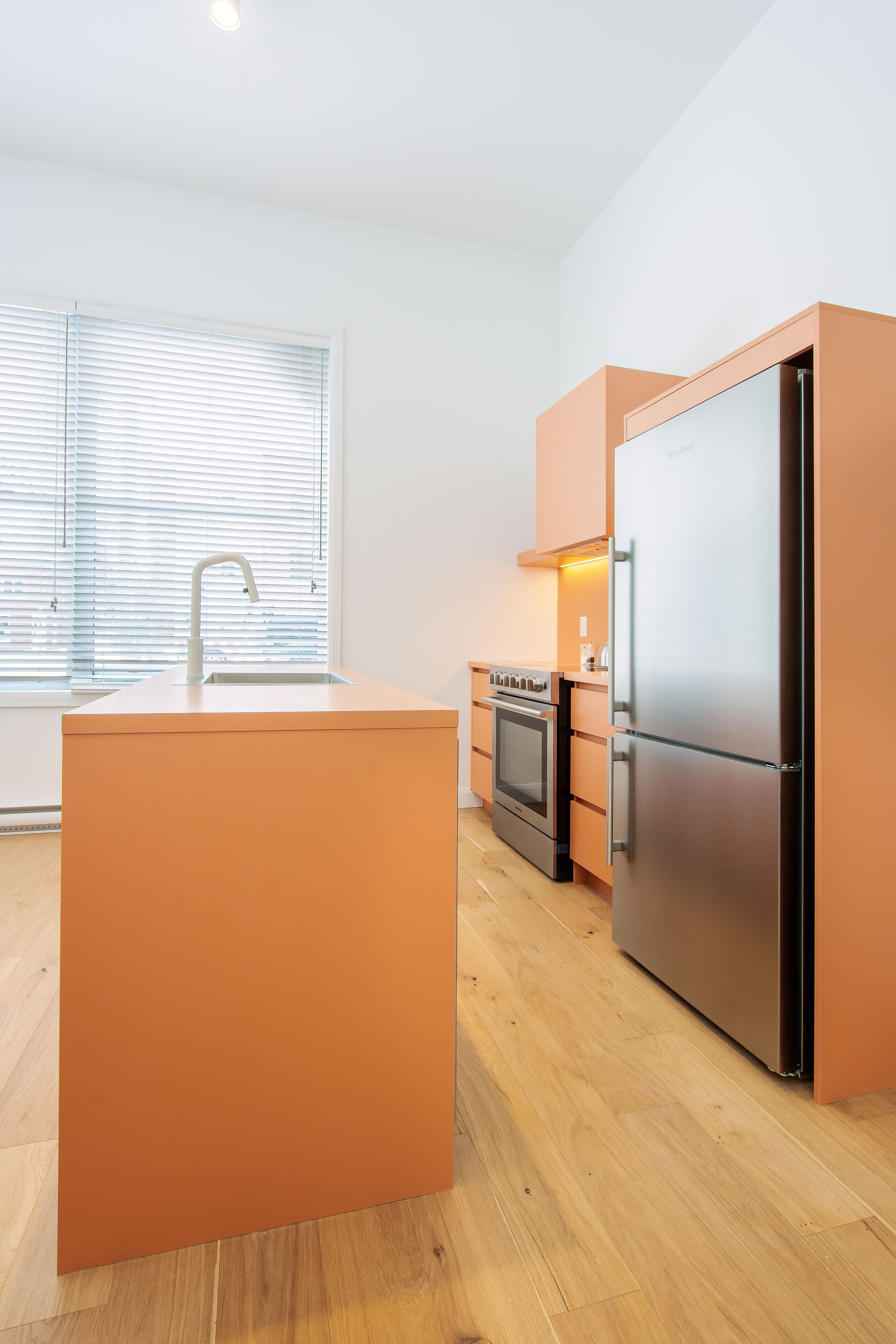 A modern kitchen with a central island, built-in oven, and stainless steel refrigerator.