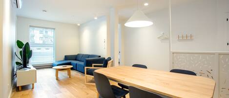 A modern living room with a wooden dining table, blue sofa, and a potted plant.