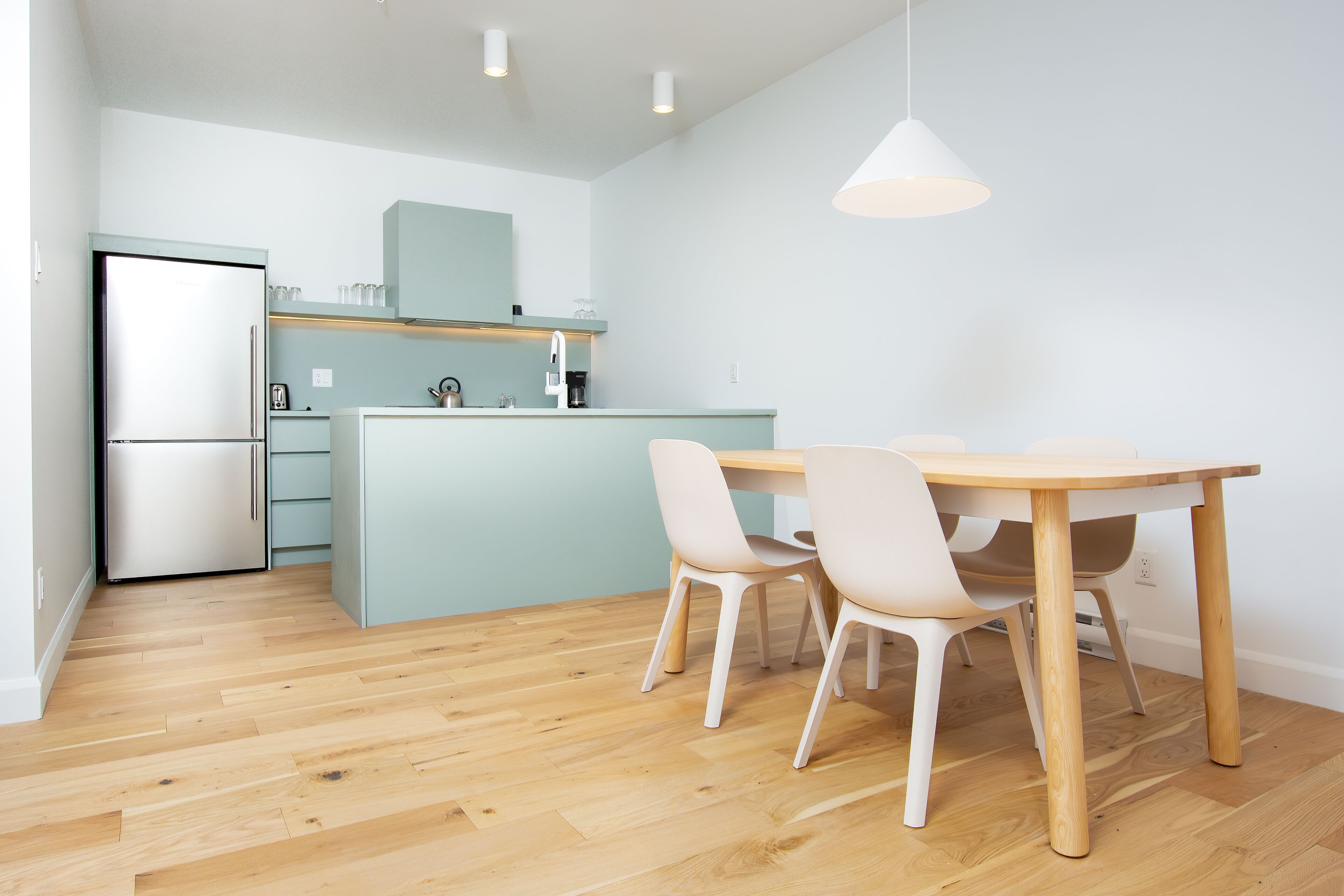 A modern kitchen with a wooden floor, a central island, and a dining area with two chairs.