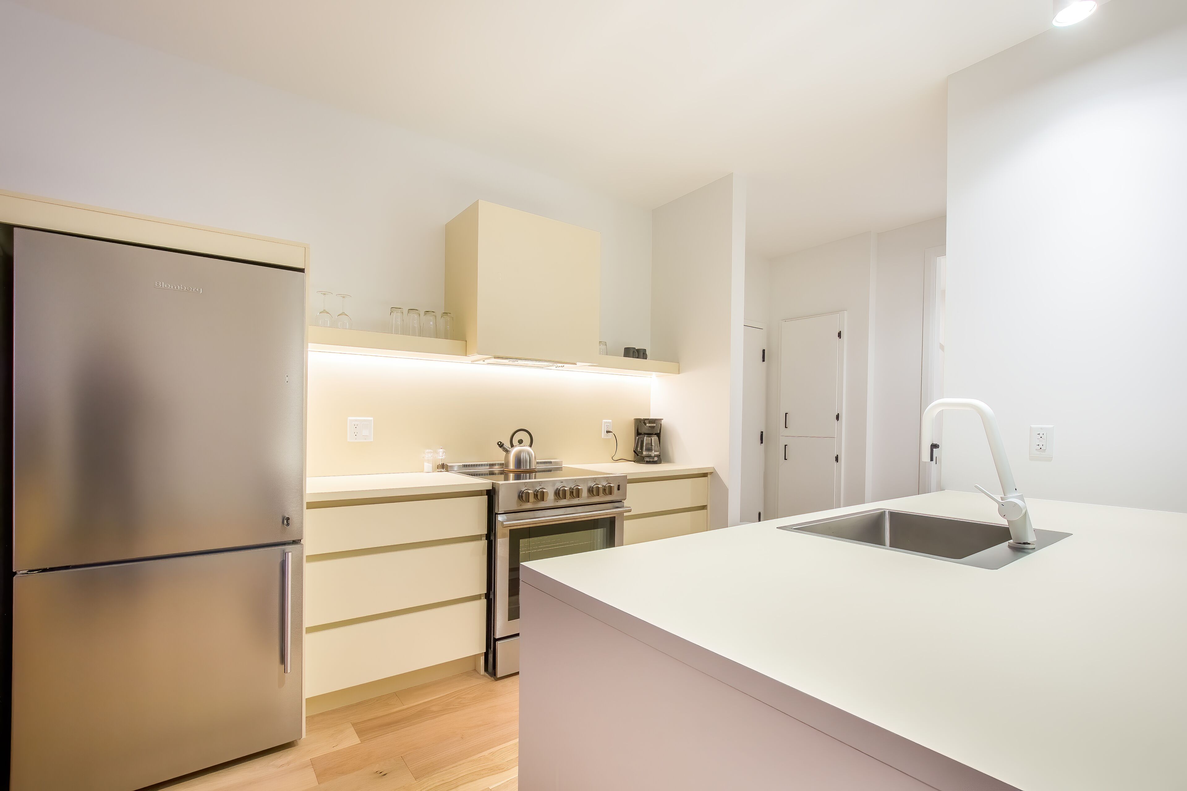 A modern kitchen with a stainless steel refrigerator, a built-in oven, and a white countertop.