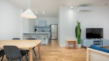 A modern kitchen with a dining area, a TV, and a large plant.